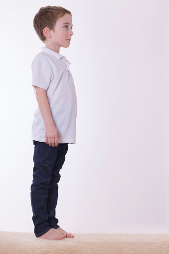Blonde little kid in striped sweater and white trousers posing in studio. Full length portrait little boy
