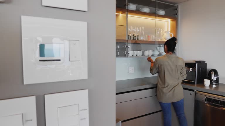 Woman making coffee in kitchen behind home automation controls