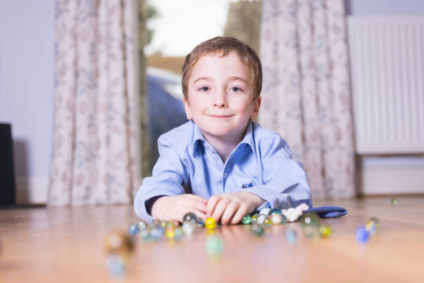 Happy small boy of 7 playing on the lounge floor with his marbles.