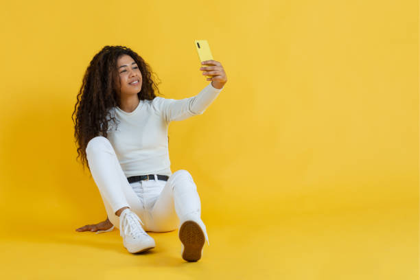 young african american woman takes a selfie with her smart phone sitting on the floor stock photo