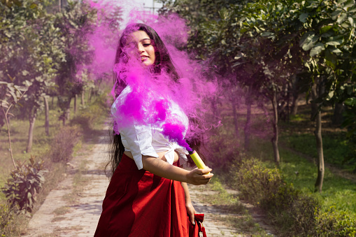 Beautiful young girl woman celebrate holi with colored multicolored smoke bombs of dry color Holi powder colour gulal abeer in the park in spring break Holi festival