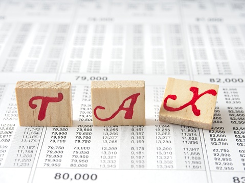 The word tax in wooden blocks with the letter X falling over, a concept of taxes falling. Toy blacks with the letter X in tax leaning over, on white over an IRS tax table.