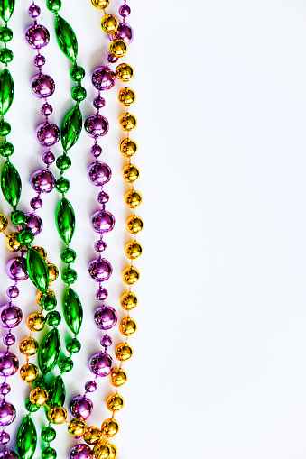 Mardi Gras background. Multicolored beads on white background. Fat Tuesday symbol. Festive decorations in gold, green and purple colors for traditional holiday. Copy space.