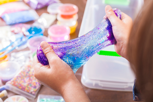 Young kids playing with colorful slime kit with glitter, toys, texture craft balls, and sparkles