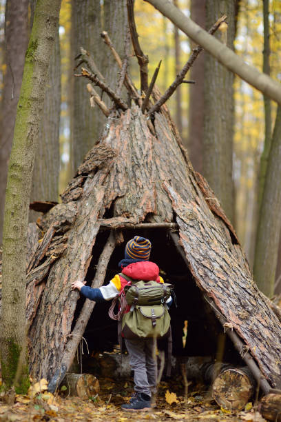 Little boy scout during hiking in autumn forest. Child examining teepee hut in woodland. Concepts of adventure, scouting and hiking tourism for kids. stock photo