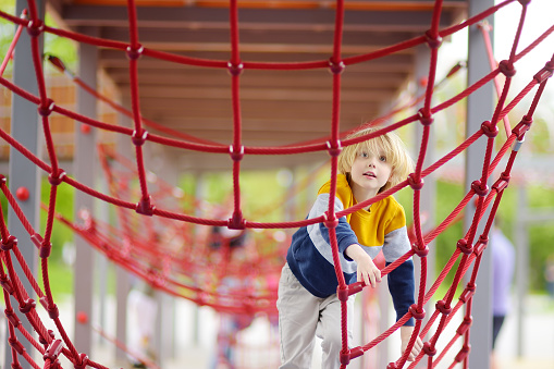 Cute preschooler boy having fun on outdoor playground. Spring summer autumn active sport leisure for kids. Activity for family with children. Equipment of entertainment park for kids.