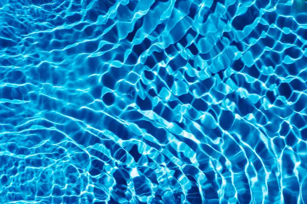 Rippled transparent fresh blue water gel surface in swimming pool with flecks, waves, shade. Healthy relaxation in sunny summer. Vacation spa coast sea, natural concept. Flat lay. Place for text