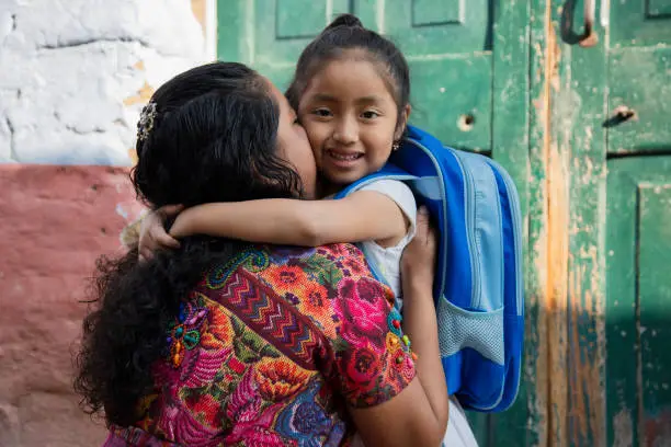 Photo of Hispanic Mayan mom hugging her little daughter ready for her first day of school-little girl with her mother ready to go to school- Back to school in Latin America
