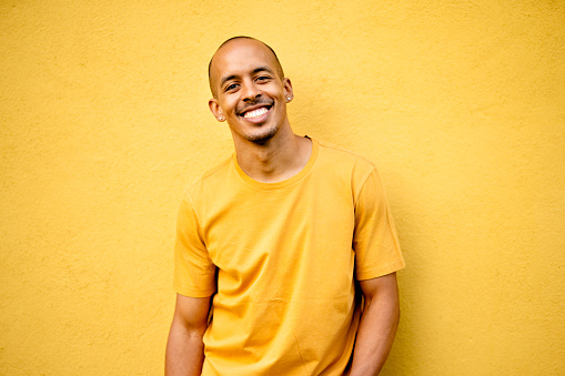 Portrait of a smiling young man wearing a yellow t-shirt leaning against a yellow wall outdoors