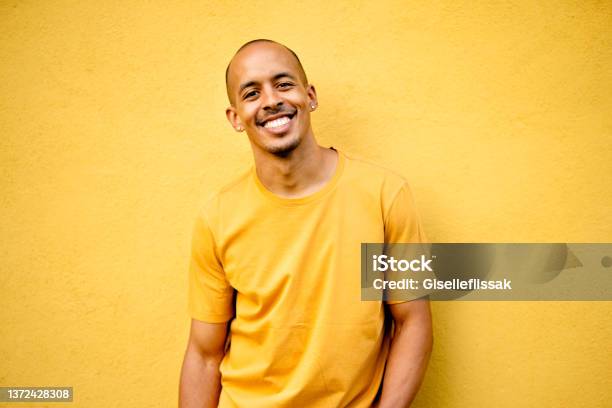 Young Man Smiling While Wearing A Yellow Shirt By A Yellow Wall Stock Photo - Download Image Now