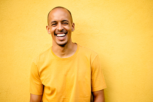 Portrait of a laughing young man wearing a yellow t-shirt leaning against a yellow wall outdoors