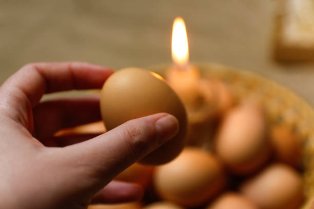 istock Hand holding egg. Candle with light. Rustic background. Paschal eggs, Pysankas. Collection of eggs on background.  Preparation for holiday. Craft paper. Tradition. Spiritual 1372429414