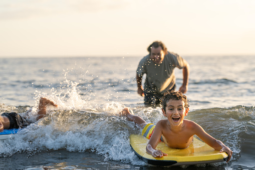 Happy boy body boarding at the beach with his dad