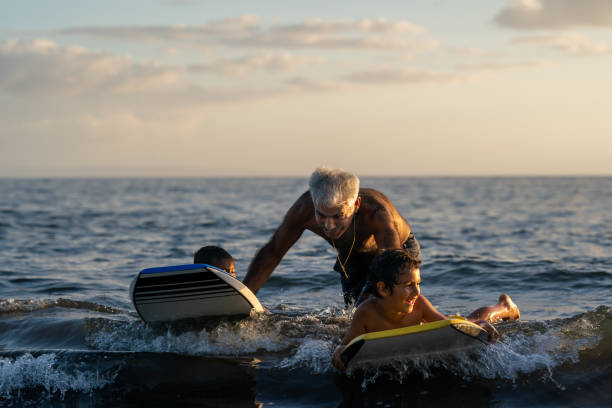 uomo anziano attivo che insegna ai suoi nipoti a body board - senior adult surfing aging process sport foto e immagini stock