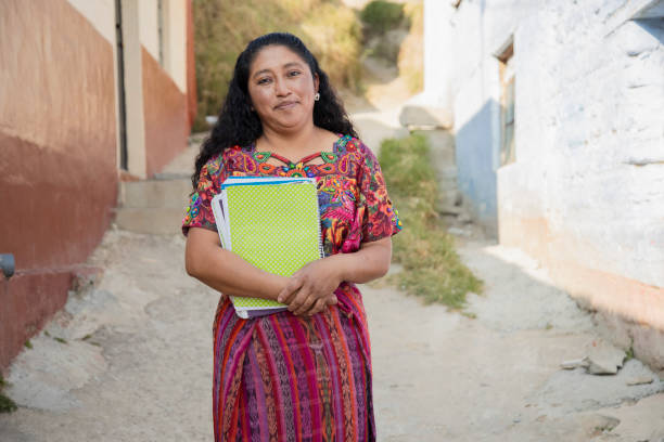 mamá hispana con cuadernos fuera de la escuela en zona rural - mujer adulta maya lista para ir a estudiar - maestra latina en la ciudad - trajes tipicos colombianos fotografías e imágenes de stock