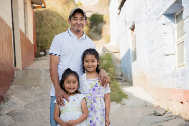 латиноамериканский отец со своими двумя счастливыми дочерьми возле своего дома в сельской местности - латиноамериканский отец обнимает св - guatemalan culture central america mother traditional culture стоковые фото и изображения