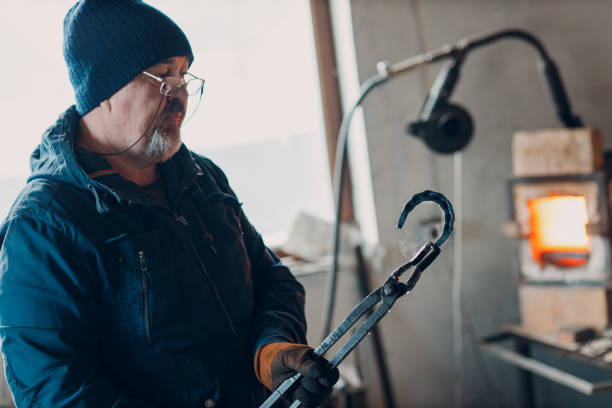 istock Blacksmith forges and tempering metal horseshoe in jar with water at forge 1372441751