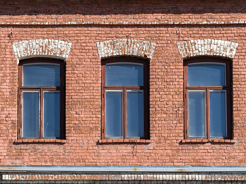 Three windows of the old mansion 19 century with brown bricks wall. Brick wall of an old 19th century building with windows.