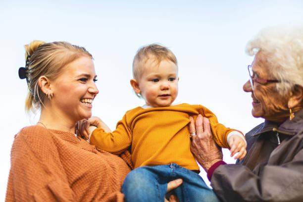 niño saltando con madre y abuela jugando juntos al aire libre en el patio a fines del verano y principios de otoño serie de fotos - child laughing blond hair three people fotografías e imágenes de stock