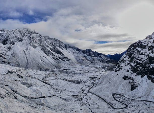 Breathtaking scenery of snowy valley with rocky mountains and curvy roads against cloudy blue sky