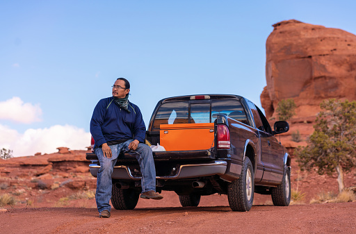 Navajo man sitting on the bed of his pick-up truck in Monument Valley