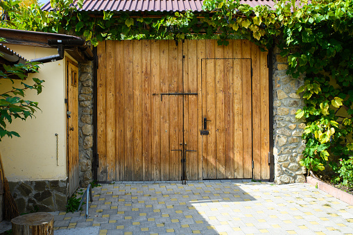 A wooden gate in a small mountain village with a wicket in one wing and twined on top with vines of grapes.