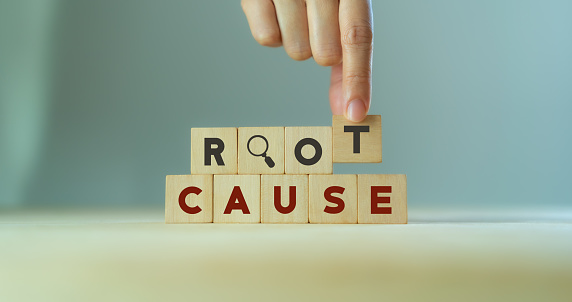 Root cause analysis concept. Define problems to find solution. Business problem solving.  Hand holds the wooden cubes with text ROOT CAUSE and magnifying glass icon on grey background,copy space.