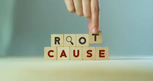 Photo of Root cause analysis concept. Define problems to find solution. Business problem solving.  Hand holds the wooden cubes with text ROOT CAUSE and magnifying glass icon on grey background,copy space.