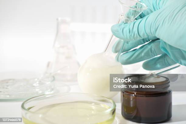 Hand In Rubber Medical Glove Holding Laboratory Glassware With Fermented Cosmetic Product Face Cream With Enzymes Developed In A Lab Stock Photo - Download Image Now
