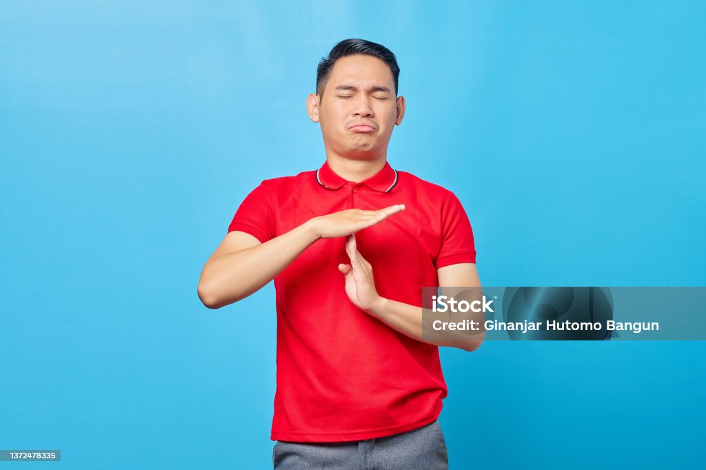Handsome young Asian man in red shirt showing time out gesture with hands isolated over blue background 25-29 Years Stock Photo