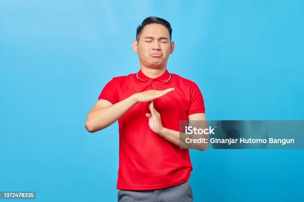 Handsome Young Asian Man In Red Shirt Showing Time Out Gesture With Hands Isolated Over Blue Background Stock Photo - Download Image Now