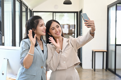 Two cheerful woman waving hand while doing video call on smart phone.