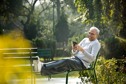 Senior man laughing while using mobile phone and relaxing at park