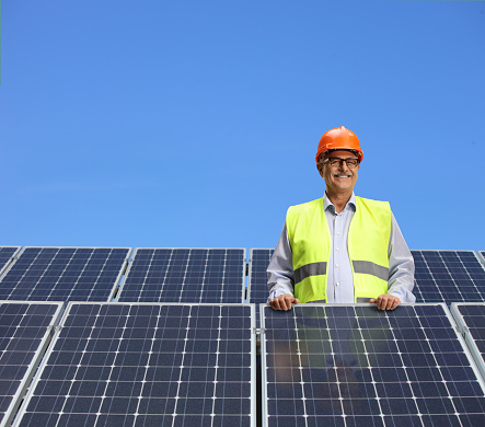 Engineer standing behind solar panels and smiling