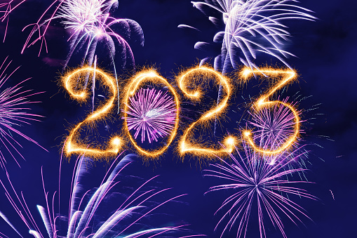 New Year fireworks and 2023 sign made of sparkler trace on a night blue sky background.