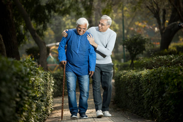 Senior man is having knee pain in the park Senior man taking care of friend suffering with knee pain while walking at the park indian man walking in park stock pictures, royalty-free photos & images