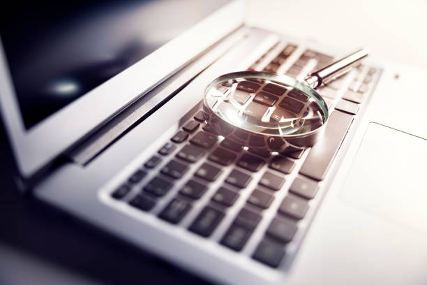 Magnifying glass on laptop keyboard searching for online documents stock photo