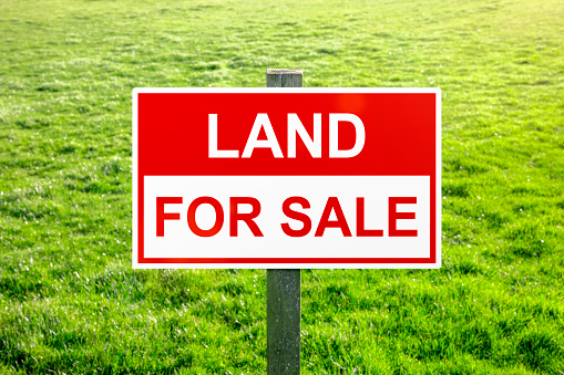 Land for sale sign in green grass field for housing development and construction background