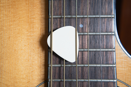 White guitar pick on an acoustic guitar