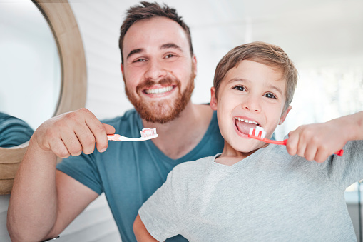 Shot of a little boy and his father brushing their teeth together at home