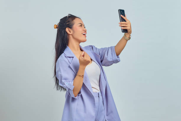 istock Cheerful young Asian woman using a mobile phone while celebrating victory on blue background 1372500108