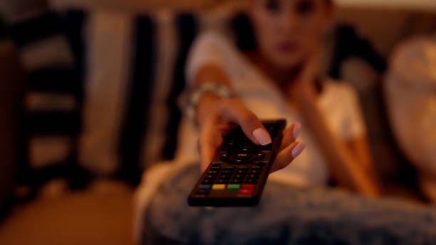 Female friends watching TV. Relaxing afternoon on a couch. Close up on hand with remote control stock photo