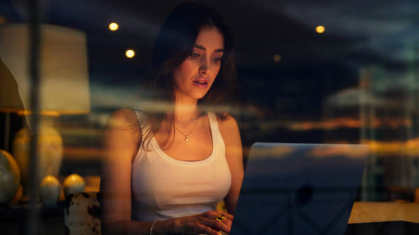 istock Businesswoman working late from home. Looking through panoramic window with sky reflections 1372500793