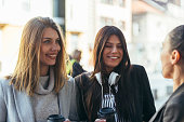 Group of girls standing outdoors and chatting with each other while drinking coffee.