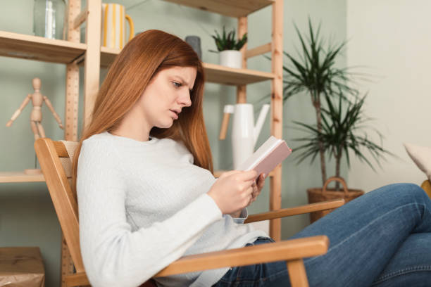 istock Young redhead woman reading a book at home 1372502467