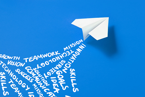 White paper plane on blue background with business related words