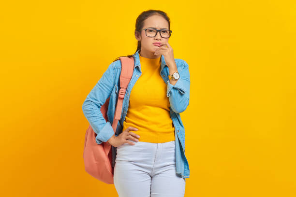 istock Beautiful young Asian student in denim outfit with backpack and looking serious thinking about question isolated on yellow background. Education in high school university college concept 1372505512
