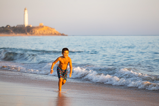 Little kid running on the beach with a lighthouse background