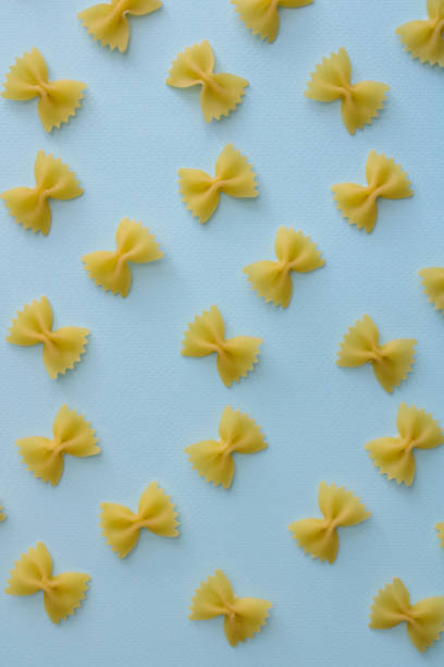 istock Pasta farfalle random flat illustration on blue background. Raw farfalle pasta on colored background 1372510874