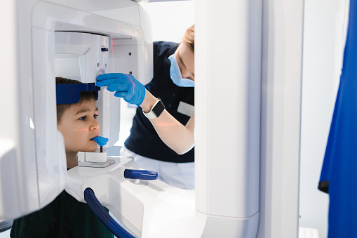 Female dentist taking panoramic teeth radiography to a little boy using modern x-ray machine